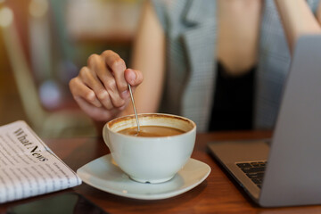 Close-up shot of coffee cup lying on table with woman's hand. Use a spoon to stir the coffee cup...