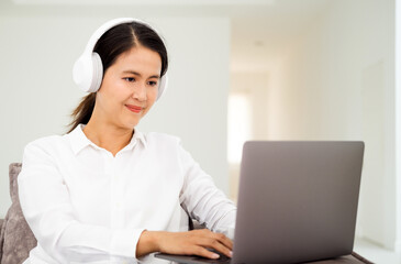 Beautiful smiling young woman in headphones chatting via laptop computer video call at home