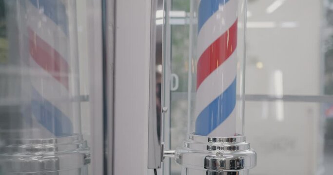 Close-up of barber's pole spinning against glass wall background of barbershop attracting client to hairdressing salon. Beauty place and objects concept.