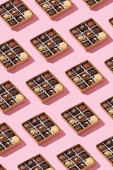 Pattern made from box with chocolate craft candies with nuts inside on pink background