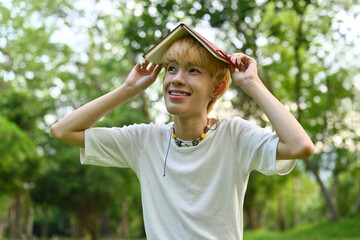 Portrait of an Asian LGBT teen boy with a book on his head smiling happily.