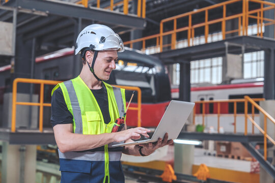 Male Maintenance Technician Team In Uniform And Safety Helmet Holding Laptop Inspecting Parts And Repairing Electric Vehicle In Electric Train Control Station