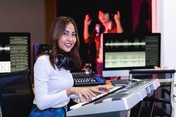 Asian producer woman in white shirt playing piano in sound studio with warm lighting background,...