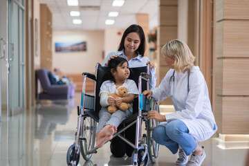 Female pediatrician doctor and child patient on wheelchair with her mother in the health medical center
