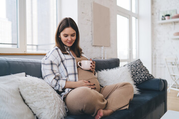 Happy pregnant woman touching belly while resting on couch