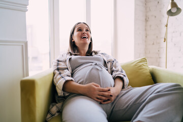 Fototapeta premium Cheerful pregnant woman resting on sofa in living room
