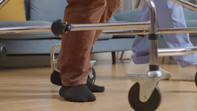 Close Up Of Male Patient'S Feet Walking By Walker Beside A Nurse Helping Him During A Physical Therapy At Home
