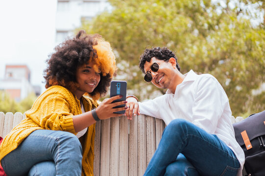 Smiling woman showing smartphone to friend on street