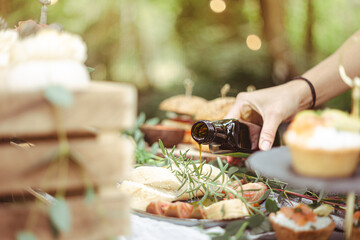 Rustic outdoor reception in elegant garden with gourmet local food. Female hand pouring virgin olive oil ove antipasti. Italian wedding
