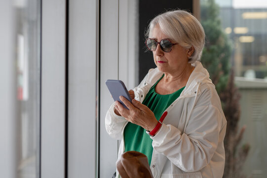 Senior woman using smartphone in hall - Powered by Adobe