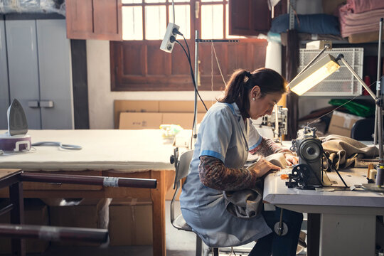 Focused female tailor sewing on machine in atelier