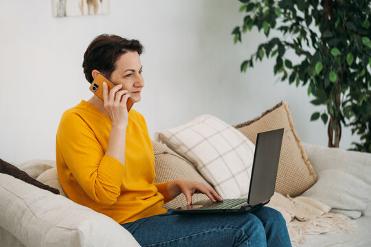Woman with laptop talking on smartphone at home