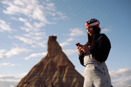Young woman browsing smartphone beside hill under blue sky