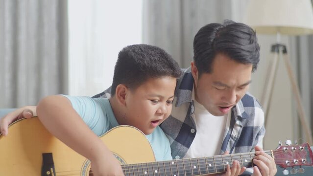 Close Up Of Happy Asian Father And Son Celebrating Be Able To Play The Guitar Together On Sofa At Home
