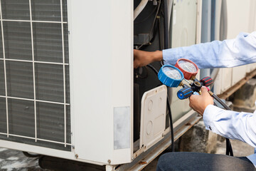 Air repair mechanic using measuring equipment for filling industrial factory air conditioners and checking maintenance outdoor air compressor unit.