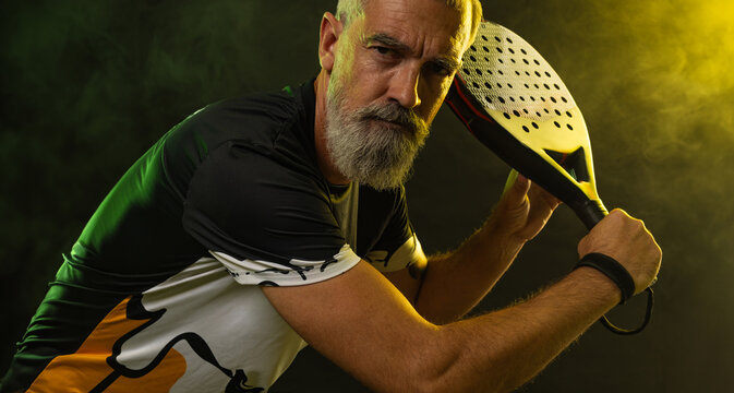 Old man. Padel tennis player with racket. Man athlete with paddle racket on court with neon colors. Sport concept. Download a high quality photo for the design of a sports app or betting site.