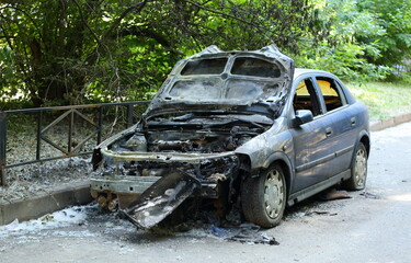 The burnt-out car is standing near a green lawn covered with poplar fluff