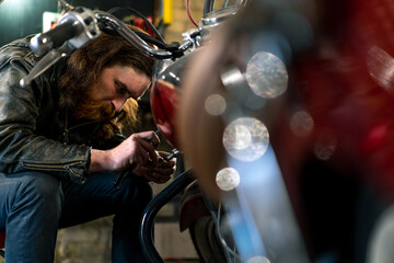 Creative authentic motorcycle workshop Garage redhead bearded biker mechanic is concentrating on repairing motorcycle