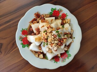 A plate of Kupat Tahu on a wooden table, is a typical food from Pacitan Indonesia which consists of rice cake, fried tofu, fried peanuts, bean sprouts, celery leaves, and sweet savory water broth.