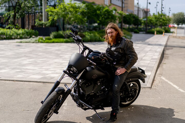 Fototapeta na wymiar brutal red-haired biker with a beard sits on a black motorcycle before the start of the race holding a helmet in his hands thirst for speed
