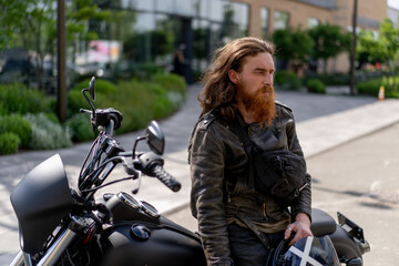 Fototapeta na wymiar brutal thoughtful redhead bearded biker sitting on a black motorcycle after a race lust for speed motorsport concept