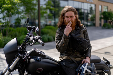 Obraz na płótnie Canvas brutal red bearded biker sitting on a black motorcycle after a race smoking a cigarette thirst for speed motorsport concept