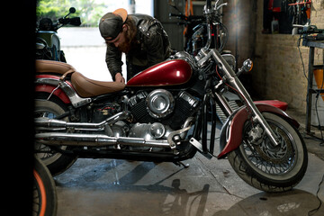 Fototapeta na wymiar Creative Authentic Motorcycle Workshop Garage Red Bearded Biker Mechanic Concentrated Repairing Motorcycle Seat
