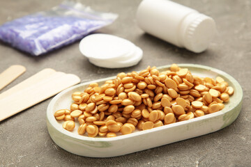 Beige wax for depilation on grey background. Wax granules for depilation. Epilation, depilation, removal of unwanted hair.