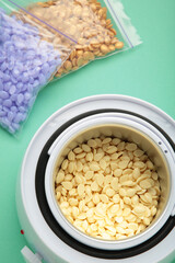 Electric wax warmer or wax heater with wax drops inside on mint background. top view.