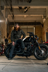 Obraz na płótnie Canvas Creative authentic motorcycle workshop garage serious redhead bearded biker mechanic sitting on motorcycle