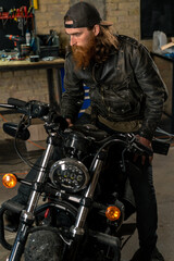 Fototapeta na wymiar Creative authentic motorcycle workshop garage portrait serious redhead bearded biker mechanic sitting on motorcycle