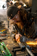 Creative authentic motorcycle workshop redhead bearded brutal biker works with circular saw Sparks...