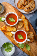 Homemade tomato soup with basil, toast and olive oil on a wooden cutting board.