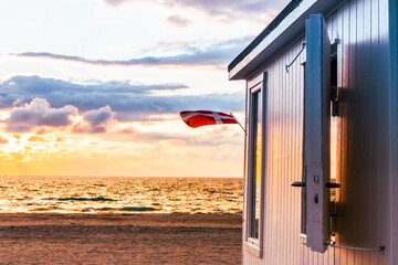 Teilansicht eines Badehauses am Strand von Løkken während des Sonnenuntergangs, eine Dänemark-Fahne weht im Wind, horizontal 