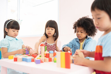 Four Multiethnic pupils playing colorful wooden blocks toy at kindergarten