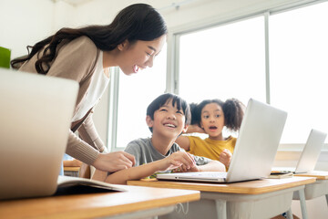Asian Female teacher helping school kids using laptop