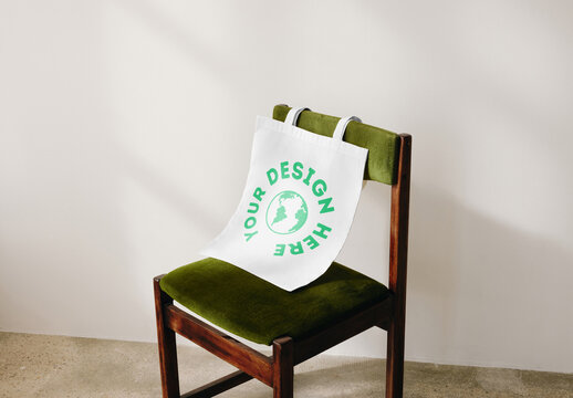Mockup of customizable tote bag hanging on back of chair