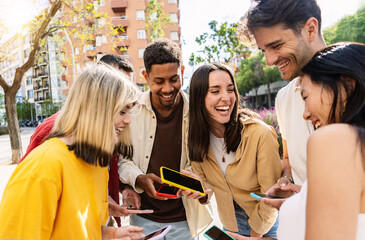 Happy group of people using having fun using smartphones at city street. Millennial generation friends laughing while watching social media content on mobile phone app. Technology concept