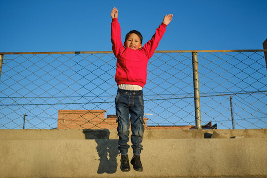 latin boy in red clothes playing with his arms up in an outdoor park in bolivia