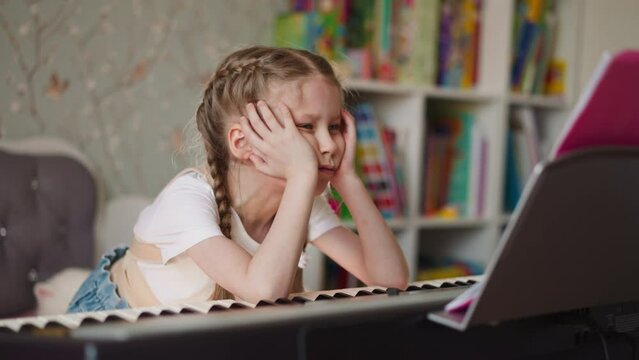 Junior schoolgirl with back braces learns musical sheets in living room. Child with spine injury sits at piano at home. Kid with backpain at music lesson