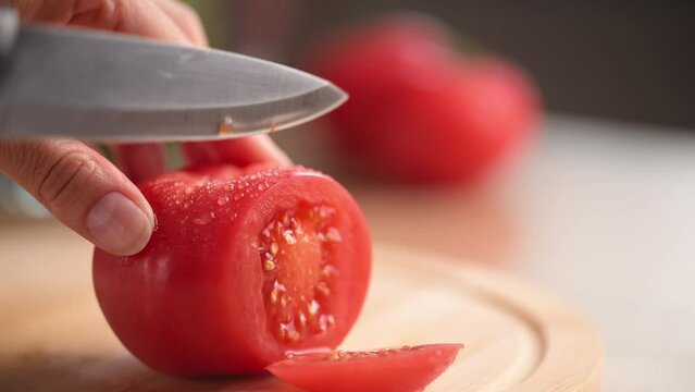 Woman cutting fresh tomato with a kitchen knife on wooden cutting board. Healthy eating. Sliced tomato on bamboo cutting board.