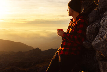 white man, mountaineer, enjoys a cup of drink while contemplating the sunset with a reflective and thoughtful gesture after a day of hiking and climbing. concept of sport, adventure and travel.
