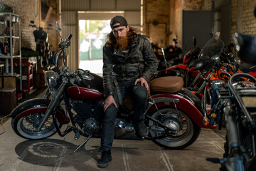 Fototapeta na wymiar Creative authentic motorcycle workshop Garage brutal serious bearded biker mechanic sitting on motorcycle