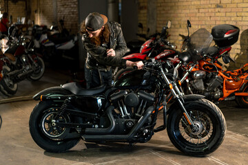 Obraz na płótnie Canvas Creative authentic motorcycle workshop Garage redhead bearded biker mechanic standing near motorcycle checking it
