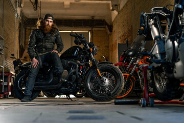 Creative authentic motorcycle workshop garage serious redhead bearded biker mechanic sitting on motorcycle