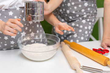 The process of sifting flour and making baking dough. A teenager's hands hold a metal cup with flour. The flour is falling.  The process of making cookies for Christmas. Family concept.