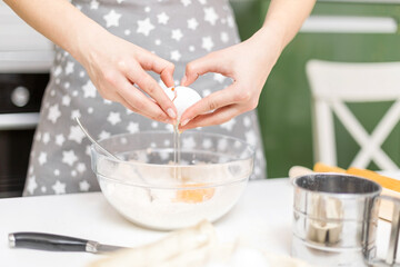 A woman's hands crack an egg into a bowl of flour at home. The process of making cookie dough.