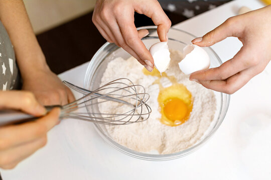 A woman's hands crack an egg into a bowl of flour at home. The process of making cookie dough.