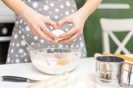 A woman's hands crack an egg into a bowl of flour at home. The process of making cookie dough.
