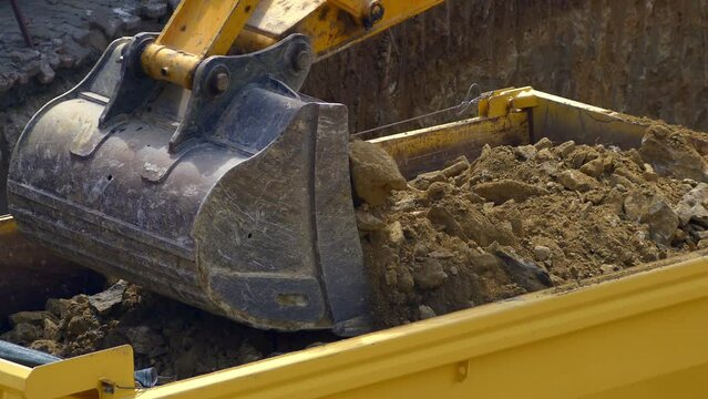 Dump truck being loaded with soil by a hydraulic excavator. Close up, UHD 4K. Excavator loader construction machine with bucket outdoors.

